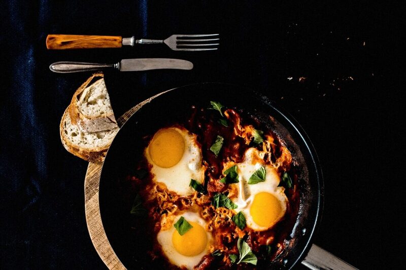 Skillet of shakshuka with poached eggs in tomato sauce, garnished with herbs