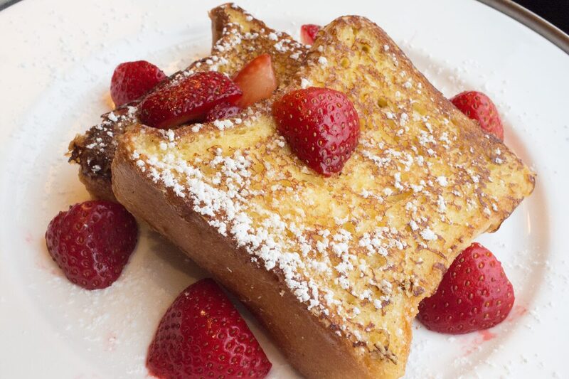 Stack of pain perdu slices dusted with powdered sugar and served with fresh strawberries