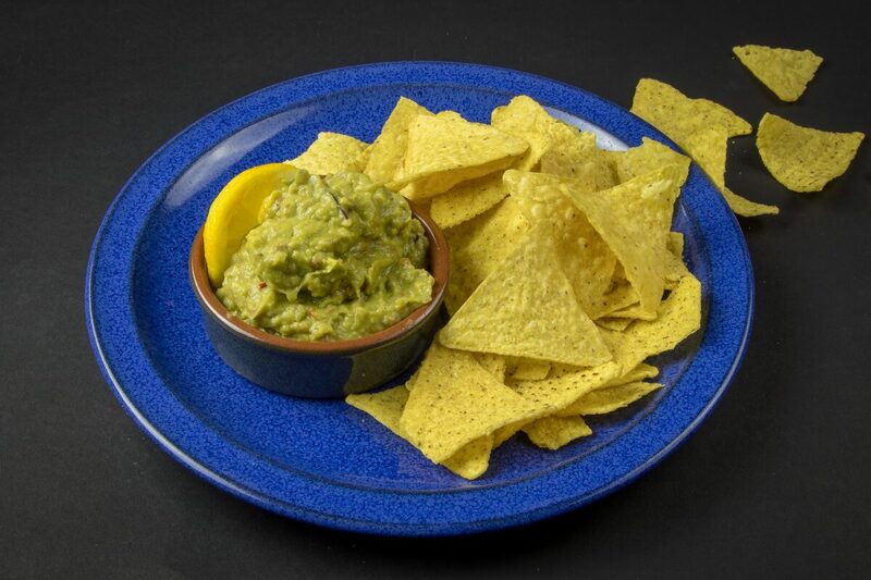 Bowl of guacamole with tortilla chips and lime wedges