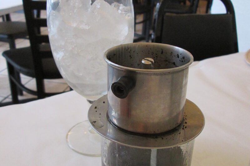 Phin filter dripping coffee into a glass, with a glass of ice on the side